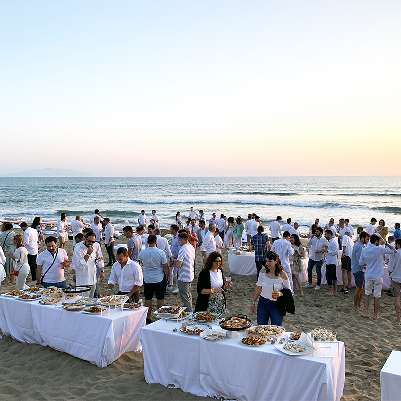 Un gruppo di persone attorno a tavoli sulla spiaggia del Garden Toscana Resort, godendosi il sole e la compagnia.